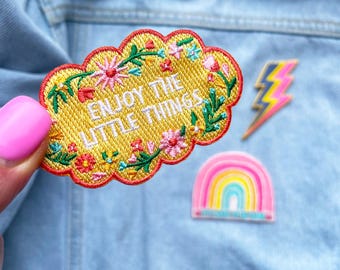 May include: Yellow embroidered patch with a cloud shape and floral details. The patch says "Enjoy the little things".