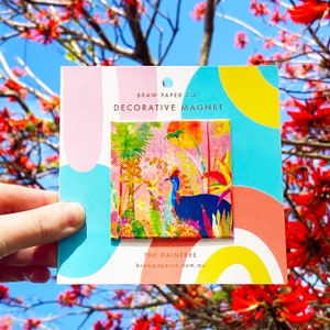 May include: A colourful magnet featuring a cassowary bird in a jungle setting. The magnet is pink, green, blue, and yellow. The text on the magnet reads "Braw Paper Co. Decorative Magnet The Daintree brawpaperco.com.au"