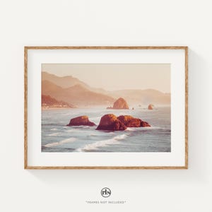May include: A photograph of a rocky coastline with a hazy, golden sunset in the background. The ocean is calm and the water is a light blue color. The rocks are a reddish-brown color and are scattered across the water.