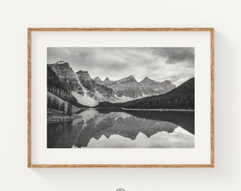May include: A black and white photograph of a mountain range reflected in a still lake. The mountains are snow-capped and the lake is calm and serene.