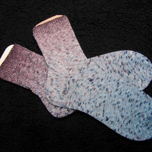 Op de afbeelding: Twee paar sokken in een blauw en paars gespikkeld patroon. De sokken liggen op een zwart, pluche oppervlak.