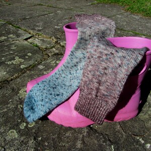 Op de afbeelding: Twee paar kleurrijke sokken in een roze rubberen laars. E&eacute;n sok is blauw en grijs met een gevlekt patroon, de andere is bruin en grijs met een gevlekt patroon.