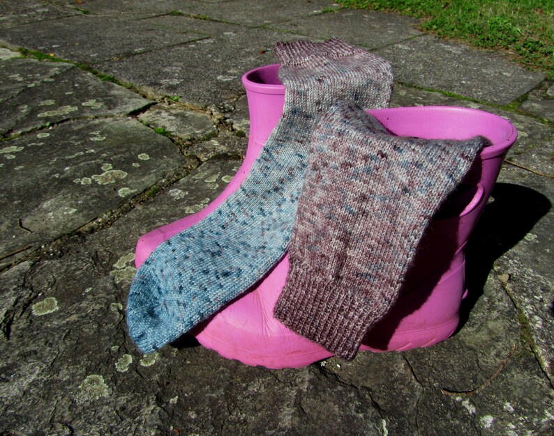 Op de afbeelding: Twee paar kleurrijke sokken in een roze rubberen laars. E&eacute;n sok is blauw en grijs met een gevlekt patroon, de andere is bruin en grijs met een gevlekt patroon.