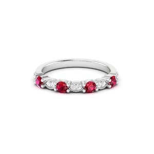 May include: A silver ring featuring a series of vibrant red gemstones alternating with smaller, clear stones. The ring has a delicate, detailed design around the stones, creating a classic and elegant look. The gemstones are round and evenly spaced.