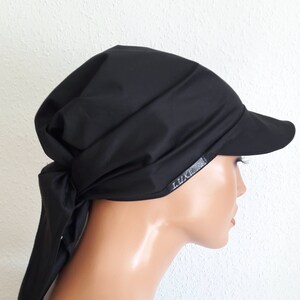 Puede incluir: Gorra visera negra con diseño drapeado y visera pequeña. El sombrero tiene una cinta en la parte trasera y una pequeña etiqueta que dice "LUXE". El sombrero está hecho de una tela negra lisa y sólida.