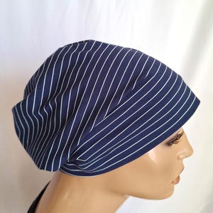Puede incluir: Un gorro azul marino con rayas verticales blancas. El gorro está hecho de una tela suave y tiene un ajuste relajado. El gorro se muestra en una cabeza de maniquí.
