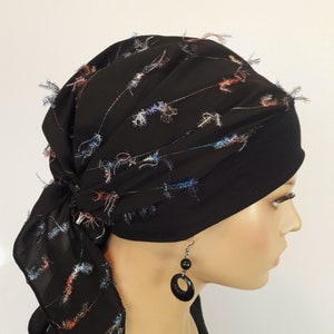 Könnte beinhalten: Schwarzes Kopftuch mit einem Muster aus farbenfrohen, fadenartigen Akzenten. Das Kopftuch ist hinten gebunden und wird mit einer schwarzen Mütze darunter getragen. Ein Paar schwarze Ohrringe hängt am Ohr.