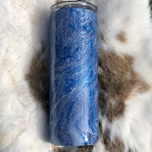May include: A blue and white glitter tumbler with a marbleized design. The tumbler has a clear lid and is made of stainless steel.