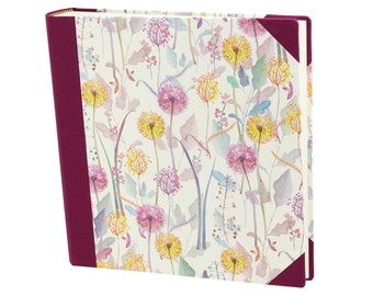 May include: A cream-colored hardcover journal with a floral pattern. The cover features a watercolor design of pink, yellow, and purple flowers with green stems. The journal has a burgundy spine and corners.