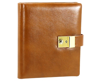 Pode incluir: Um diário de couro castanho com um fecho dourado. O diário é retangular e tem um acabamento liso e brilhante. O fecho é retangular com um pequeno buraco de fechadura e uma correia de couro.