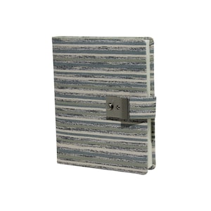 May include: A hardcover journal with a striped pattern in shades of gray, blue, and beige. The journal features a metal clasp closure and a matching fabric strap. The edges of the journal are white.