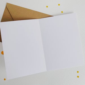 K&ouml;nnte beinhalten: Eine leere wei&szlig;e Karte mit einem braunen Umschlag. Die Karte ist in der Mitte gefaltet und hat eine leere Innenseite. Der Umschlag ist aus braunem Papier und hat eine strukturierte Oberfl&auml;che.