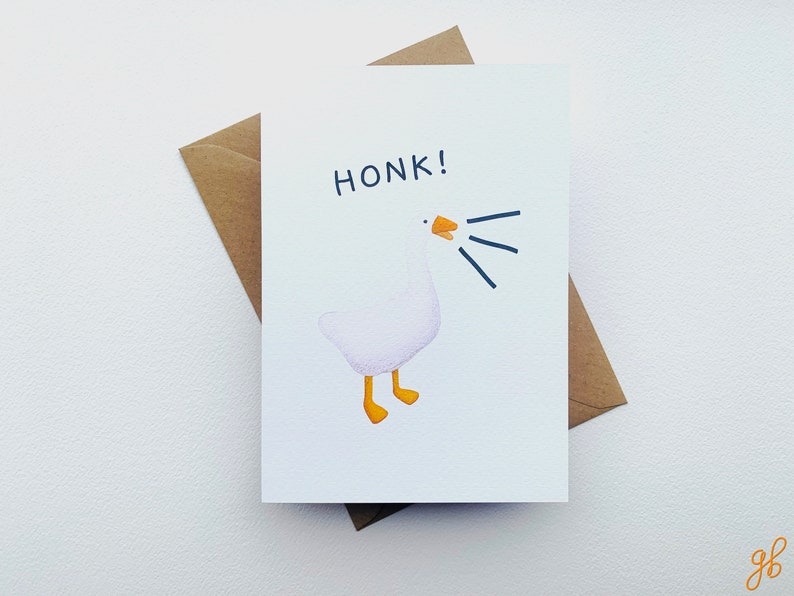 Może przedstawiać: Biała kartka z pozdrowieniami z ilustracją z kresk&oacute;wki przedstawiającą gęś. Gęś gęga, z napisem &bdquo;HONK!&rdquo; nad nią. Gęś ma ż&oacute;łte stopy i ż&oacute;łty dzi&oacute;b. Karta jest połączona z brązową kopertą.