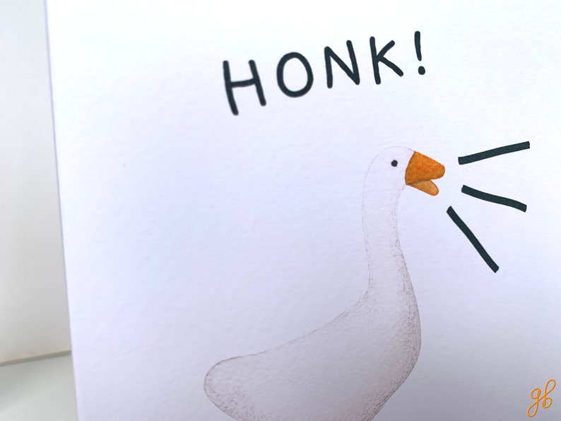 Może przedstawiać: Ilustracja białej gęsi z pomarańczowym dziobem i napisem "HONK!" czarnym tekstem. Czarne linie wychodzą z dzioba gęsi, sugerując dźwięk gęgania. Grafika znajduje się na białym tle.