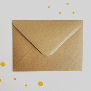 K&ouml;nnte beinhalten: Ein brauner Papierumschlag auf wei&szlig;em Hintergrund mit gelben Konfetti, die um ihn herum verstreut sind.