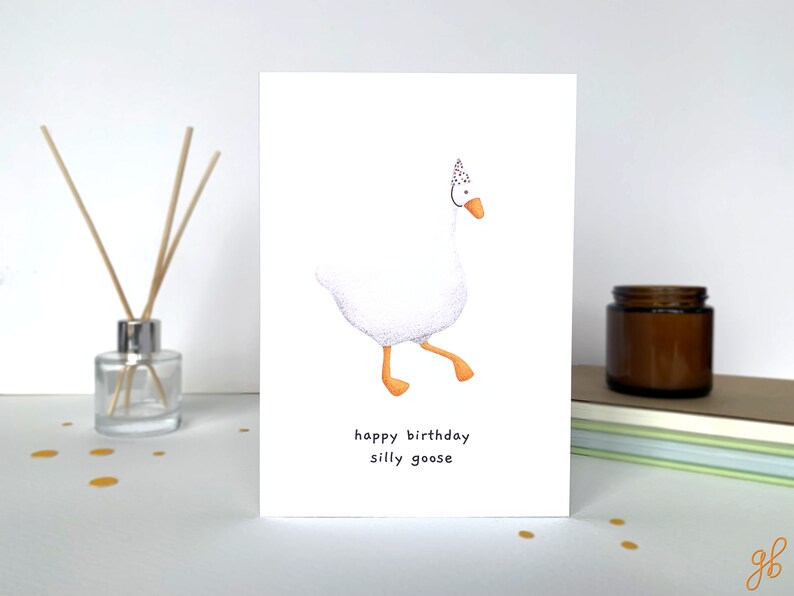 K&ouml;nnte beinhalten: Eine wei&szlig;e Gans mit einer roten und wei&szlig;en Partym&uuml;tze mit Punkten geht nach rechts. Der Text "happy birthday silly goose" befindet sich unter der Gans.
