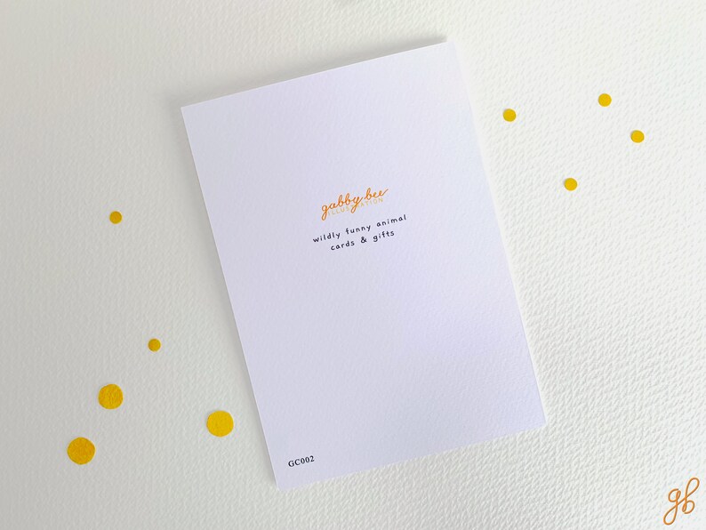 Może przedstawiać: Biała kartka z pozdrowieniami z pomarańczowym tekstem "gabby bee illustration" i "wildly funny animal cards & gifts". Karta leży na białej powierzchni z ż&oacute;łtymi kropkami. Widoczny jest kod "GC002".