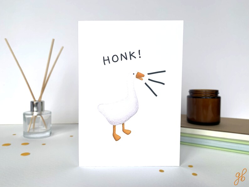 Może przedstawiać: Biała kartka z ilustracją z kresk&oacute;wki przedstawiającą gęś i słowem "HONK!" w kolorze czarnym. Gęś ma pomarańczowe stopy i dzi&oacute;b, z czarnymi liniami wskazującymi dźwięk. Kartka leży na białej powierzchni.