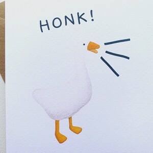 Może przedstawiać: Biała kartka z pozdrowieniami z akwarelową ilustracją gęsi. Gęś gęga, z napisem "HONK!" nad nią. Gęś ma pomarańczowe stopy i dzi&oacute;b. Brązowa koperta znajduje się po lewej stronie.