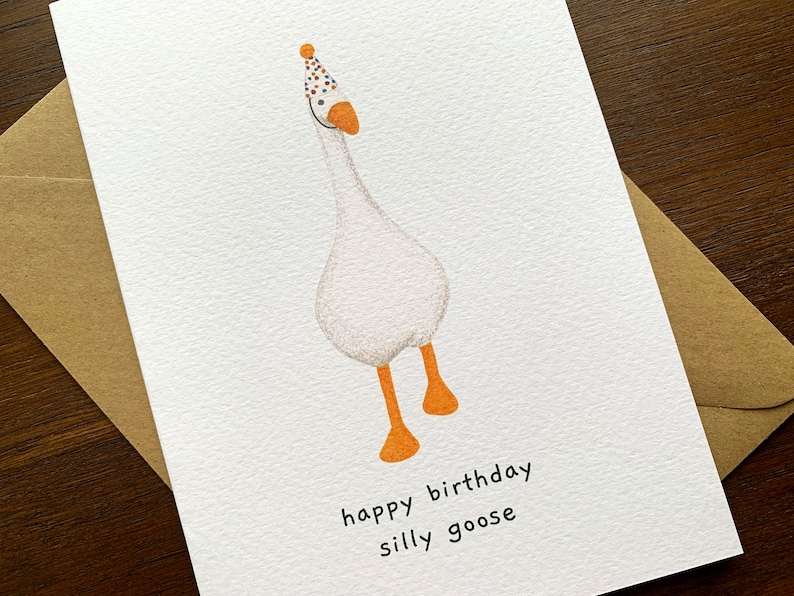 May include: A white goose wearing a colorful party hat with the text "happy birthday silly goose" on a white card.