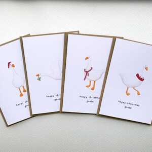 May include: Four Christmas greeting cards featuring illustrations of white geese with festive accessories. Each card has a different goose design, including a Santa hat, a sprig of mistletoe, and a scarf. The text "happy christmas geese" is printed on each card.