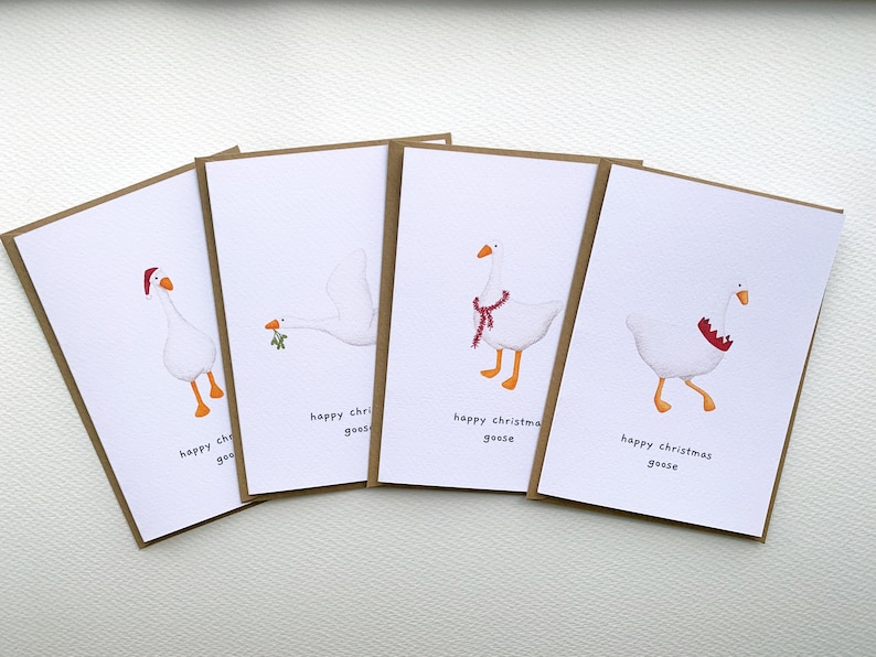 May include: Four Christmas greeting cards featuring illustrations of white geese with festive accessories. Each card has a different goose design, including a Santa hat, a sprig of mistletoe, and a scarf. The text "happy christmas geese" is printed on each card.