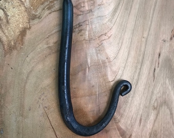 May include: A black metal hook with a simple, curved design. The hook is made of forged iron and has a rustic, handmade look.