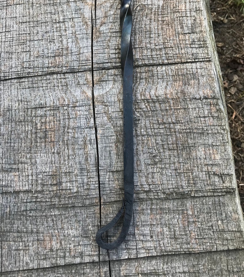 Może przedstawiać: Czarny metalowy poker do kominka ze skręconym uchwytem i pętlą na końcu.