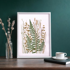 May include: A white framed print with a pressed fern and dried flowers on a white background.