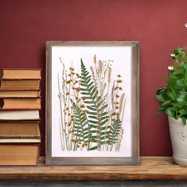 May include: A framed pressed flower art piece featuring a variety of green ferns and dried grasses with brown seed heads on a white background.