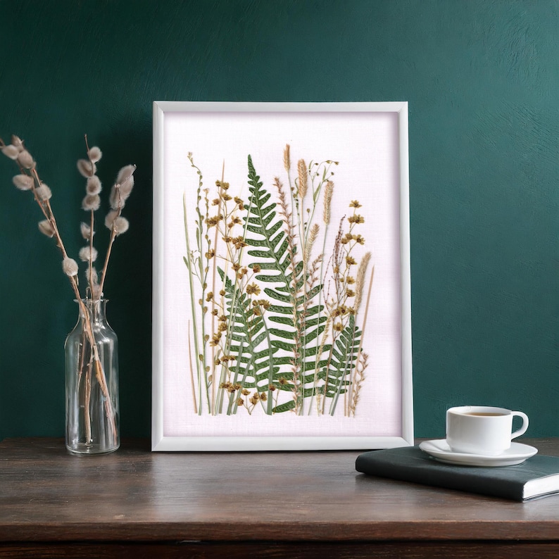 May include: A white framed print with a pressed fern and dried flowers on a white background.