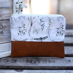 Könnte beinhalten: Ein rechteckiger Beutel mit einem weißen oberen Bereich mit einem botanischen Druck von Schmetterlingen, Blättern und Beeren. Der untere Bereich ist braun. Der Beutel hat einen Reißverschluss.
