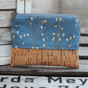 Könnte beinhalten: Eine kleine blaue Reißverschlusstasche mit Korkboden. Die Tasche hat ein weißes Blumenmuster und der Text "Faden-madchen" ist an der Seite sichtbar.