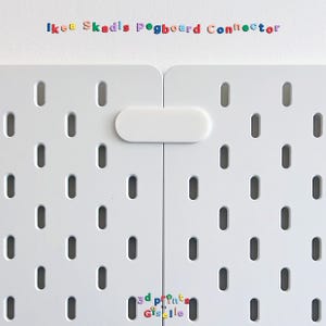May include: A white plastic connector piece joining two white pegboards with vertical oval slots. The text 'Ikea Skadis Pegboard Connector' appears at the top, and '3d prints by Giselle' is printed near the bottom centre of the pegboard panels.