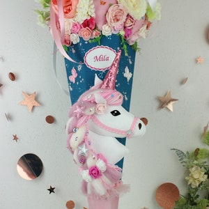 Könnte beinhalten: Ein rosa-blauer Schultüte, verziert mit einem Einhorn, Blumen und Schmetterlingen. Die Schultüte hat ein Namensschild mit dem Namen "Mila".