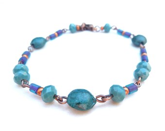 Copper-colored bracelet with various types of glass and wooden beads in petrol, green and purple colors