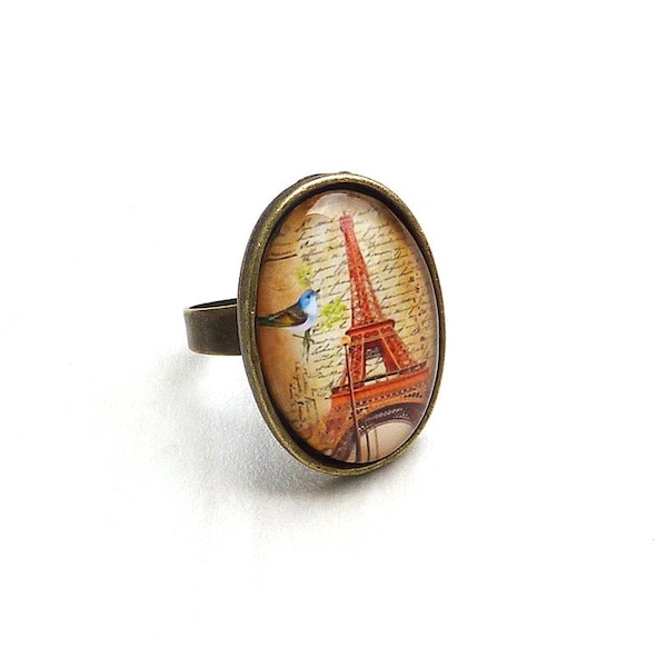 Bague parisienne en métal couleur bronze ornée d'un cabochon en verre et d'une Tour Eiffel orange à fond d'oiseau et texte manuscrit.