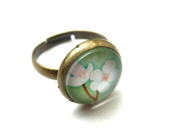 Graceful ring with a glass cabochon of white flowers on a light green background. The size of the ring is adjustable in size