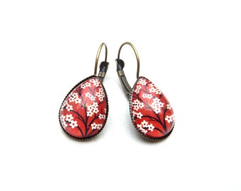 Bronze-colored earrings with glass cabochon and white flowers with black stems on a red background