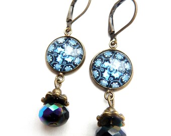 Une sorte de boucles d'oreilles bleues avec un cabochon en verre, un fond bleu foncé et une illustration blanc/bleu de poissons et d'étoiles