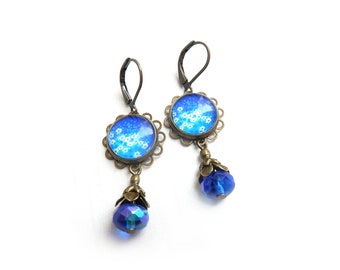 Boucles d'oreilles Brocante avec un cabochon en verre à fleurs blanches sur fond bleu, terminé par des perles de verre bleues transparentes