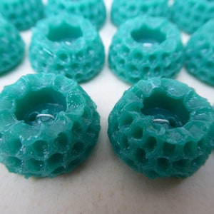 May include: A collection of teal blue, round, decorative buttons with a honeycomb pattern and a small hole in the center.