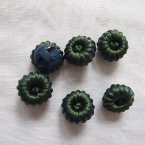 May include: Six green and blue fabric covered buttons with a raised center. The buttons are arranged in a semi-circle on a white background.