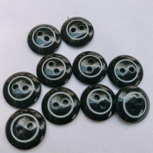 Può includere: Una collezione di dieci bottoni neri con un anello bianco e due fori bianchi al centro.