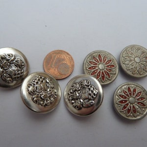 May include: A collection of vintage silver-toned buttons. Some buttons feature ornate, raised designs, while others have a red and silver floral pattern. A Euro coin is included for size comparison. These buttons are ideal for sewing and craft projects.