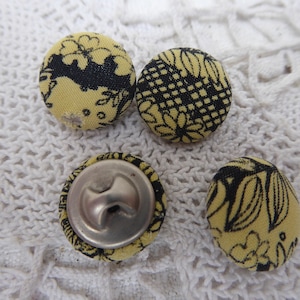 May include: Four yellow fabric buttons with black floral designs. One button has a silver metal shank.