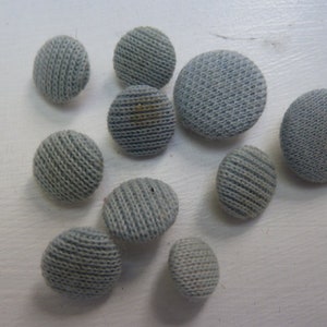 May include: A collection of ten light blue fabric buttons with a textured surface.