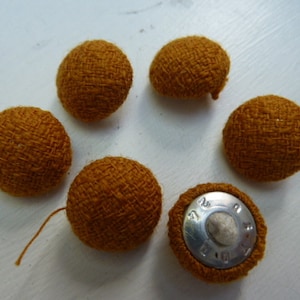 May include: Six brown fabric buttons with a silver button with the text "77 101" in the center.