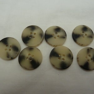 May include: Seven round, cream-colored buttons with black swirl patterns and four holes each.