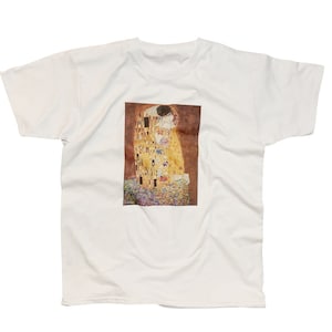 May include: White t-shirt featuring a print of Gustav Klimt's "The Kiss" painting. The painting depicts two figures embracing in a golden mosaic style.